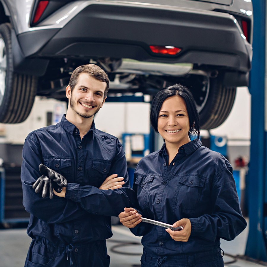 Auto car repair service center. Two happy mechanics - man and woman standing by the car