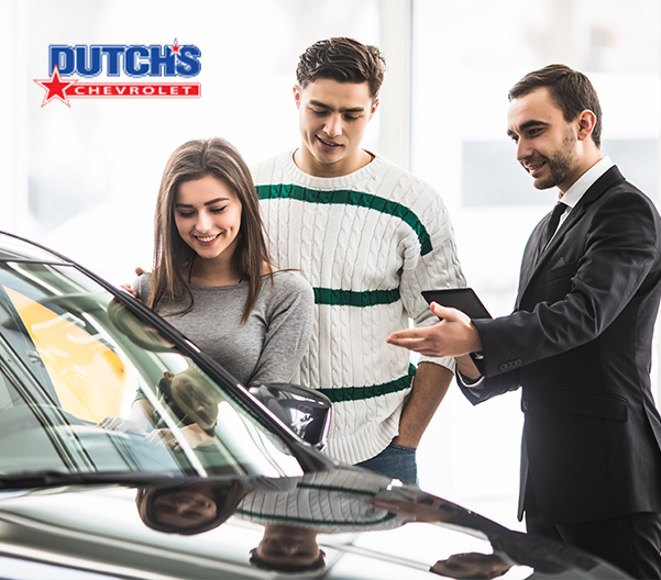 salesperson showing customers a new car at a dealership