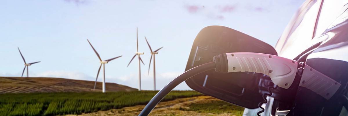 Electric vehicle parked charigng in front of a group of wind turbines.