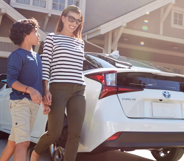 Woman and child walking next to a Toyota with a residential house in the background