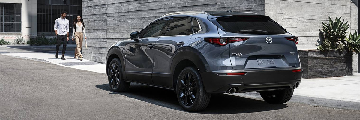 3/4 rear view of the 2024 Mazda CX-30 Crossover SUV parked with two people walking towards the car