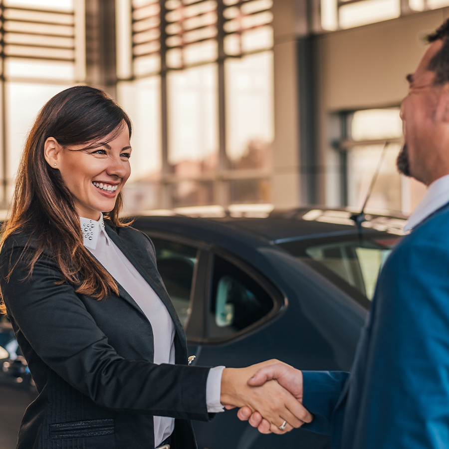 Cheerful car dealer handshake with customer in showroom.
