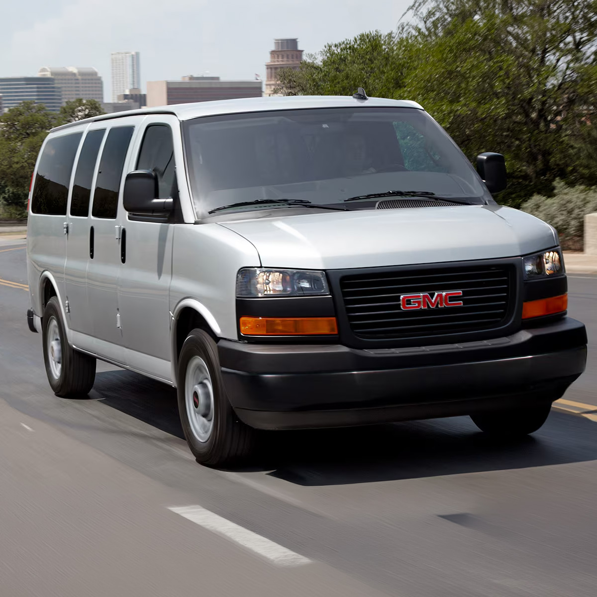Wide Front Three-Quarters View of a 2026 GMC Savana Passenger Van Driving on an Empty Road